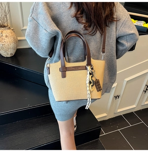 Detail of a brown textured crossbody bag with leather handles and decorative charms