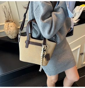 Detail shot of a beige canvas shoulder bag with brown leather trim and tassel on a model