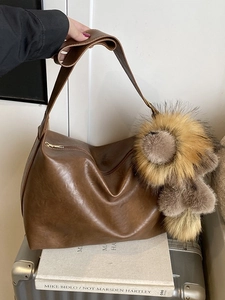 Retro dark brown leather tote bag with a fuzzy plush charm on a silver suitcase