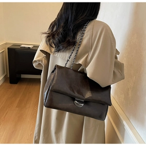 Detail der dunkelbraunen Leder-Tote mit silberner Kettenriemen auf beigem Trenchcoat