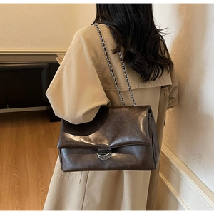 Detailansicht der kaffeebraunen Ketten-Tasche mit glänzender Öl-Leder-Textur an der Schulter