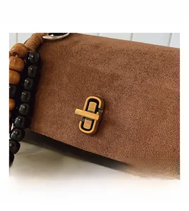 Close-up of brown suede small square bag with golden turn-lock and beaded strap details
