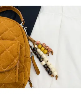 Détail d'un sac bandoulière matelassé marron avec une breloque amovible en perles