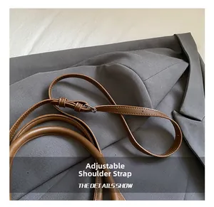 Detail of adjustable shoulder strap and silver metal buckle on a brown leather bag