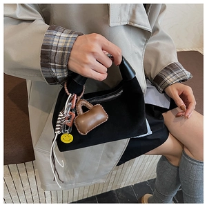 Detail der schwarzen Wildleder-Mondtasche mit gelbem Smiley-Anhänger und Mini-Etui