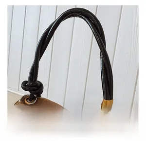 Detail of brown suede handbag featuring twisted black leather handles and wooden bead accents