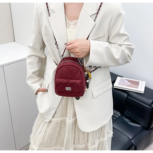 Détail d'un mini sac à dos matelassé en velours bordeaux avec chaîne et pendentif perlé