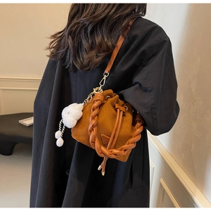 Détail du sac seau en daim marron avec poignée tressée et charm nuage blanc sur manteau