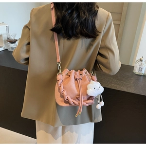 Détail d'un sac seau rose mat avec poignée tressée et breloque nuage en peluche au café