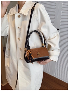 Detail of vintage suede handbag with T-shaped gold lock and wooden bead charm on a trench coat