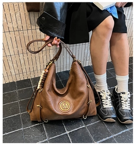 Detail of vintage brown tote bag with metallic M logo and beaded pendant charm