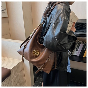 Detail of vintage brown leather tote bag with gold M logo and decorative wood beads