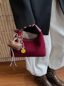 Burgunderfarbene Wildleder-Schultertasche mit Fransen und Anhängern an einem Model