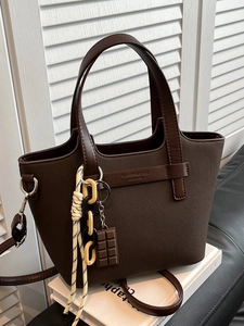Dark brown leather tote bag with cross pattern and stylish hanging charm on white book