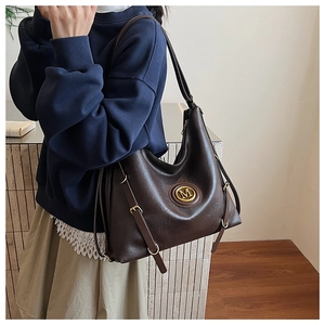 Detail of dark brown leather hobo bag featuring a gold metal M logo and side buckles