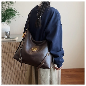 Detail of vintage brown tote bag with gold M-logo and decorative beaded charm