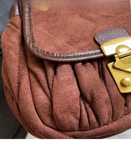 Detail of brown pleated suede shoulder bag featuring a golden metal push-lock closure