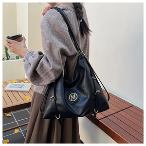 Detail of a black textured tote bag featuring a metallic M logo in an urban lifestyle setting