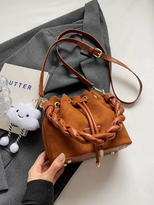 Sac seau en daim marron avec poignée tressée et charm nuage sur fond de costume gris