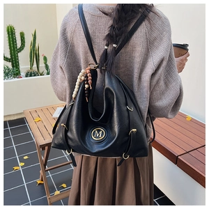 Detail of black glossy leather tote featuring a metal M logo and ethnic beaded charm
