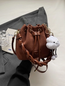 Sac seau en daim marron avec bandoulière tressée et charm nuage sur fond de blazer gris