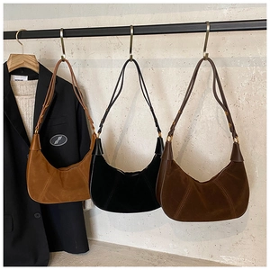 Trois sacs demi-lune en daim marron, noir et café suspendus à des cintres métalliques