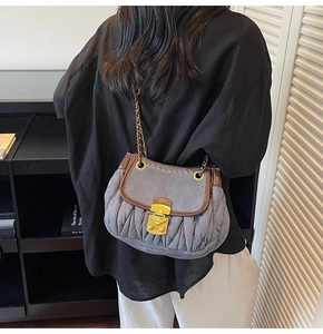 Detail of gray pleated denim bag with vintage gold buckle and leather trim on model