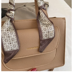 Close-up of light brown lychee grain leather handbag with silk scarf detail and gold logo
