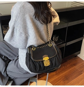 Detail of black pleated shoulder bag featuring gold clasp and leather chain strap