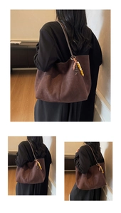 Detail of a large dark brown suede tote bag with ethnic beaded tassel charm on a shoulder strap