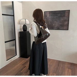 Detail of dark brown leather shoulder bag with woven strap and round charm on model