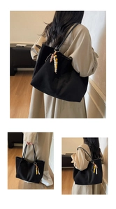 Detail of a black large-capacity canvas tote bag with colorful beaded tassel pendant accents