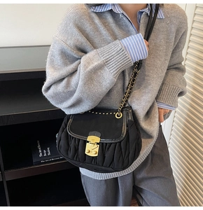 Detail of black pleated shoulder bag with vintage gold lock and chain strap on model