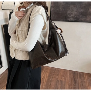Detail of a large brown leather hobo bag featuring a decorative baseball charm and strap