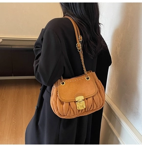 Detail of caramel suede bucket bag with gold studs and metal chain strap on black coat