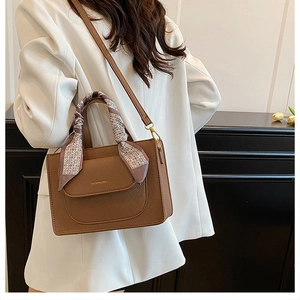 Close-up of brown litchi leather handbag with floral silk scarf wrapped on the handle