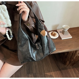Close-up of black hobo shoulder bag with a vintage baseball glove charm and braided rope