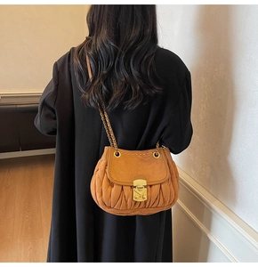Detail of tan suede pleated shoulder bag with gold clasp and chain strap on a model