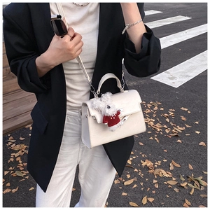 Detail of a creamy white handbag with a plush toy charm in a stylish urban street setting