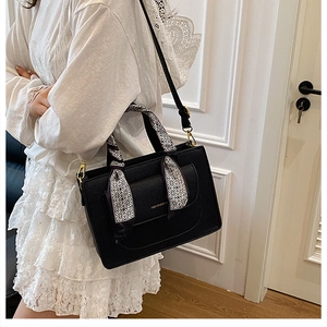 Close-up of black lychee texture tote bag featuring silk scarf handle and golden lettering