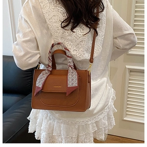 Brown lychee leather tote with silk scarf handle and gold lettering on white lace dress