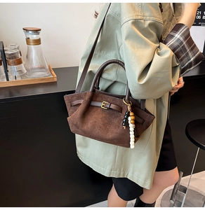 Detail view of brown matte suede handbag with stylish bead charm and gold buckle accents