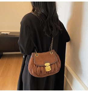 Brown suede pleated bag with gold chain strap shown on model in a high-quality lifestyle shot