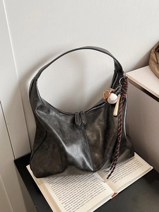 Vintage large dark grey hobo bag with baseball charms on a minimalist book background