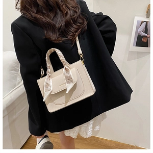 Detail of a beige structured handbag with silk scarf handle and detachable shoulder strap