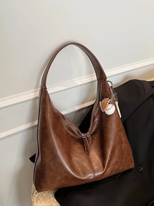 Retro dark brown hobo bag with baseball charm and textured leather in a minimalist setting
