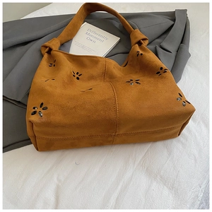 Detail of laser-cut flower patterns on brown suede shoulder bag with spacious interior