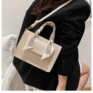 Close-up of beige lychee leather handbag with silk scarf handle and gold text detail