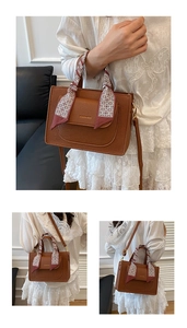 Detail of caramel leather handbag with decorative scarf handle and gold fashion lettering
