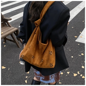 Detail of caramel suede tote bag featuring laser-cut floral patterns and knotted shoulder strap